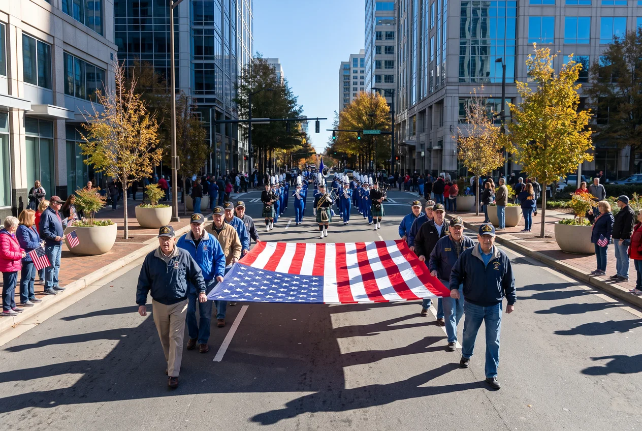 Veterans in unit ball caps marching south down Tryon Street through Uptown Charlotte on a clear November morning, glass towers on both sides and spectators with small American flags